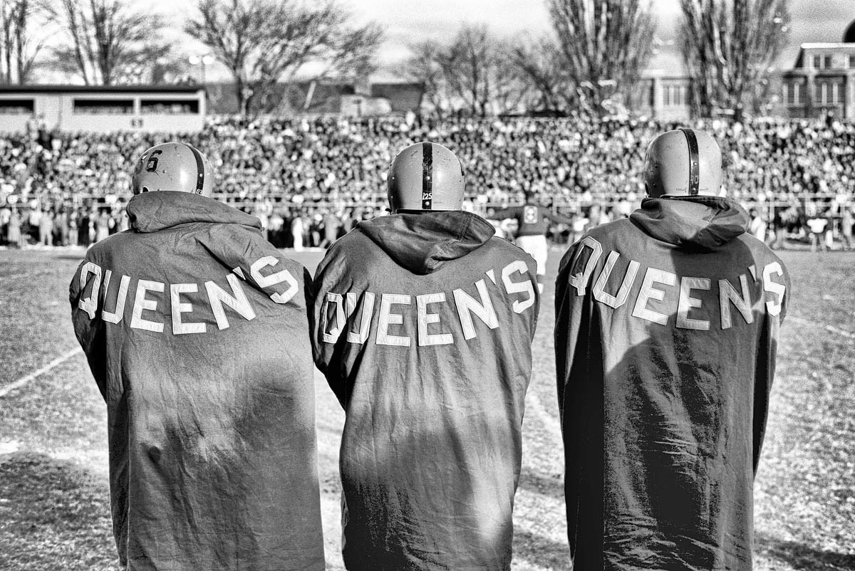 black/white photo of football players with Queen's on back of jerseys