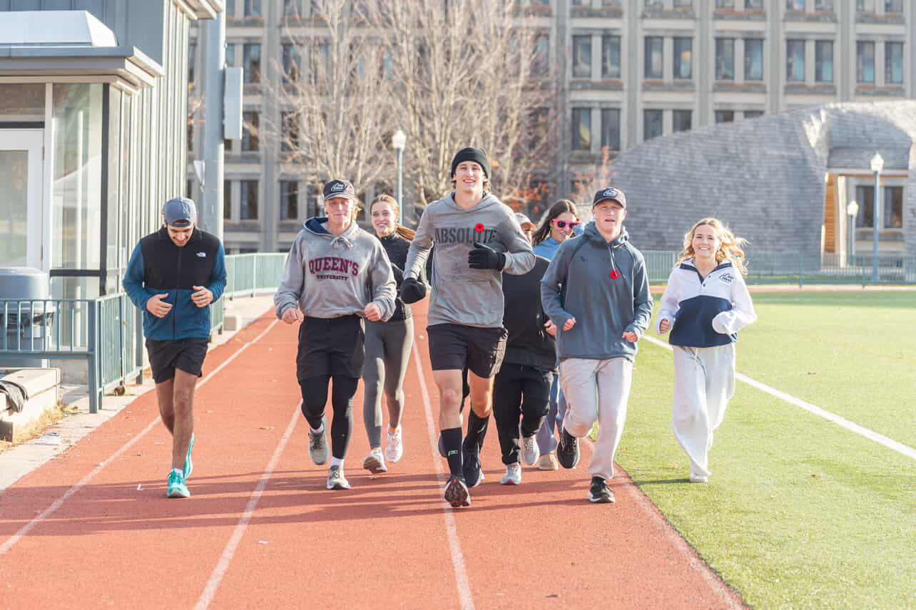 A group of people are running around a race track outside. They are in a group and look very happy.