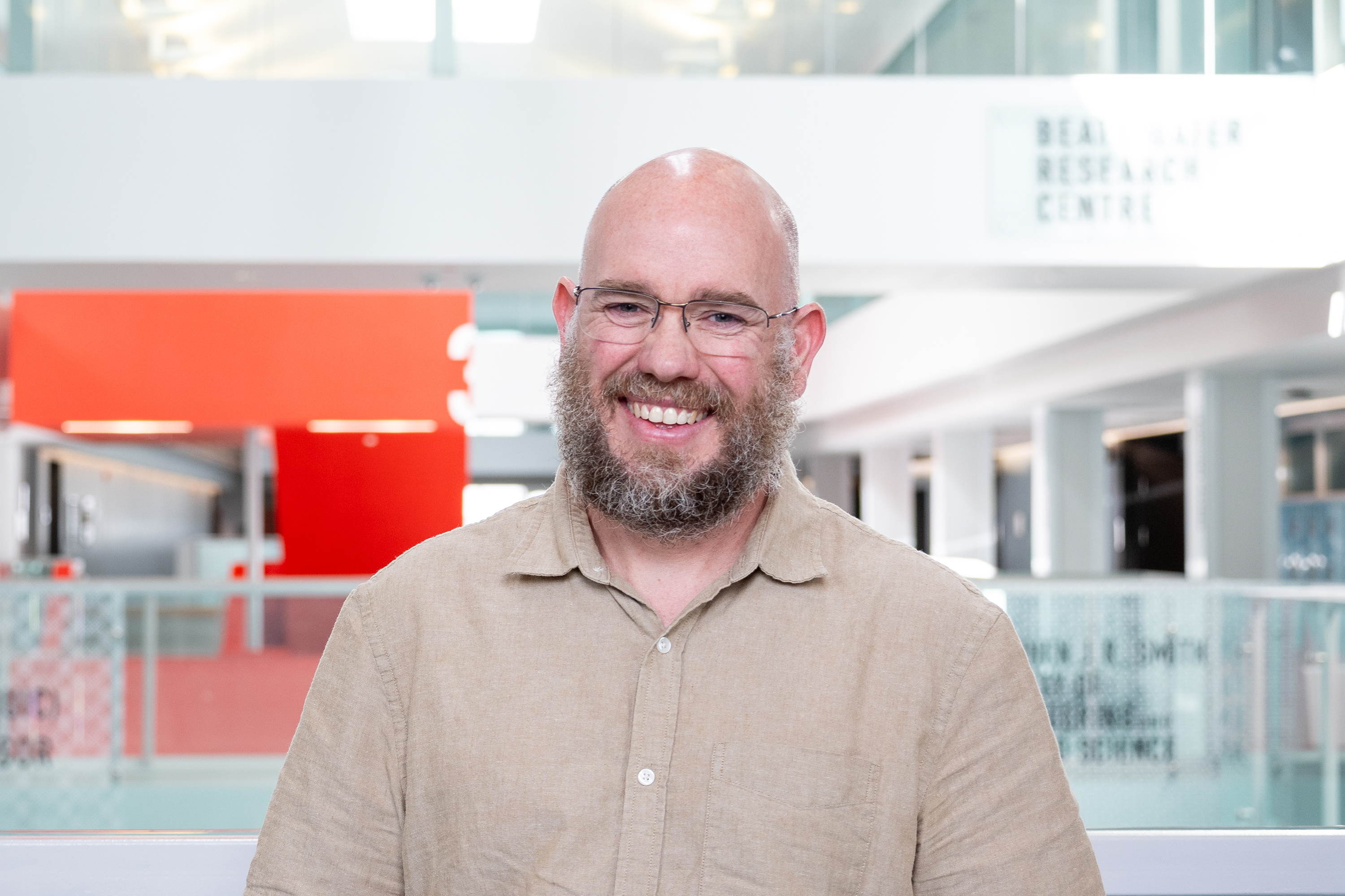 Caucasian man with beard and glasses smiling at camera. It is a professional headshot